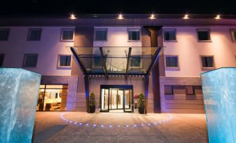 a modern building with a glass entrance and a large glass canopy is illuminated by blue lights at Winter Garden Hotel Bergamo Airport