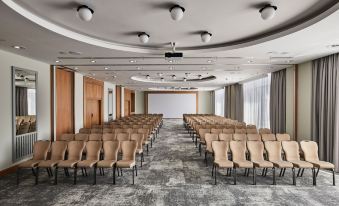 a large conference room with rows of chairs arranged in a semicircle , and a projector screen mounted on the wall at Sheraton Poznan Hotel