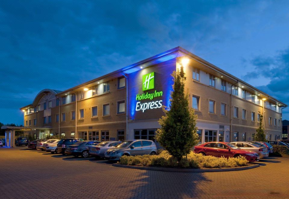a large building with a holiday inn express sign on the front , surrounded by cars and parking lots at Holiday Inn Express East Midlands Airport