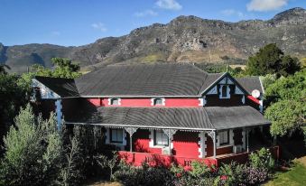 a red and black house surrounded by a lush green garden , with mountains in the background at Ruby Rose