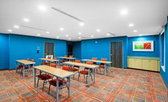 a conference room with multiple tables and chairs , blue walls , and a television mounted on the wall at Home2 Suites by Hilton Gonzales