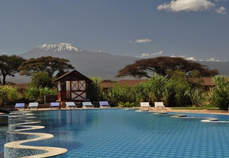 a swimming pool with lounge chairs and a gazebo in front of a snowy mountain at Kilima Safari Camp