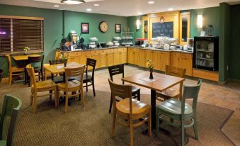 a restaurant with wooden tables and chairs , a large kitchen area , and a clock on the wall at AmericInn by Wyndham Anamosa