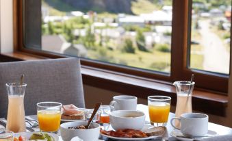 a table is set with plates of food , glasses of orange juice , and a view of mountains outside at Los Cerros del Chalten Boutique Hotel