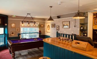 a pool table and bar area in a restaurant , with a blue counter and wooden stools at The Swan Inn