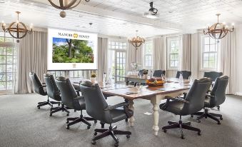 "a conference room with a large table , chairs , and a projector screen displaying the "" manor house "" logo" at Manoir Hovey