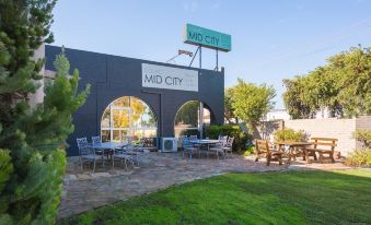 "a black brick building with a sign that says "" mid city "" and a patio area with tables , chairs , and umbrellas" at Colac Mid City Motor Inn