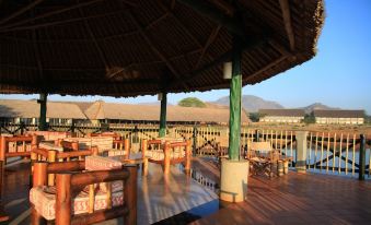 a large wooden structure with thatched roof , surrounded by various tables and chairs on a deck , providing a view of the outdoors at VOI Wildlife Lodge