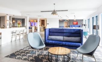 a modern lounge area with a blue couch , wooden coffee table , and gray chairs in the background at Hampton by Hilton Humberside Airport