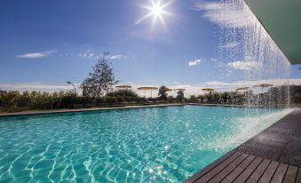 a large outdoor swimming pool surrounded by grass and trees , with people enjoying their time in the pool at Monchique Resort & Spa