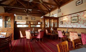 a cozy restaurant with wooden walls , red carpeted floor , and various dining tables and chairs arranged for guests at Best Western Plus Pastures Hotel