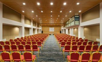 a large conference room with rows of red chairs arranged in a semicircle , and a projector screen mounted on the wall at Duja Bodrum