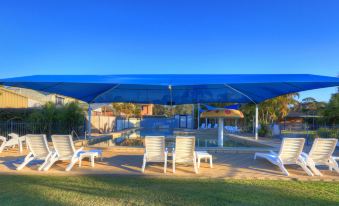 a large outdoor area with white lounge chairs , umbrellas , and a view of the ocean at Nambucca River Village by Lincoln Place