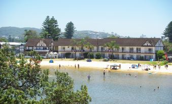 a group of people enjoying a day at the beach , with some swimming in the water and others playing in the sand at The Clan Terrigal
