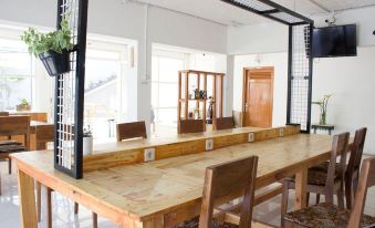 a wooden dining table surrounded by chairs in a room with large windows and a metal mesh screen at Tani Jiwo Hostel