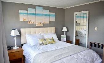 a cozy bedroom with a white bed , two nightstands , and a painting on the wall at Friars Bay Inn & Cottages