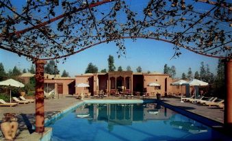 a large outdoor swimming pool surrounded by a brick building , with several lounge chairs and umbrellas placed around the pool area at Al Moudira Hotel