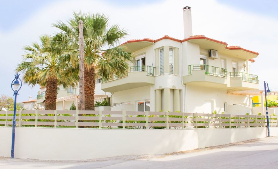 a two - story house with a white exterior , surrounded by palm trees and a picket fence at Minthi Boutique Apartments