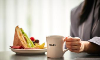 A person is sitting at a table, with their hand on top and holding up an iced beverage at HOMES Stay Myeongdong