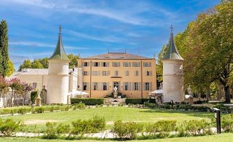 a large yellow building with two towers is surrounded by a lush green lawn and trees at Chateau de Fonscolombe