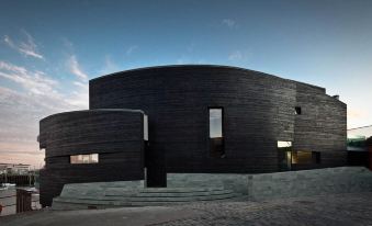 a modern , curved black building with large windows and a stone exterior , set against a clear blue sky at Rocksalt