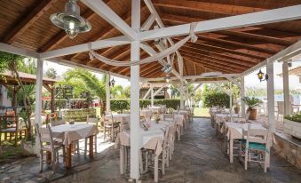 a well - decorated outdoor dining area with white tables and chairs under a wooden roof , surrounded by lush greenery at Apollo Apartments