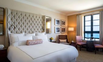 a large bed with white linens is in a room with a pink chair and framed pictures on the wall at Condado Vanderbilt Hotel