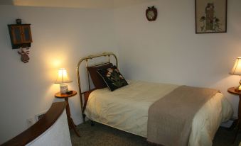 a bed with a gold headboard and white sheets is next to a small table with a lamp at Dreamcatcher Bed and Breakfast