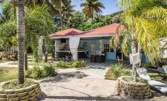 a blue house with a red roof is surrounded by palm trees and has a patio area in front of it at Solace by the Sea