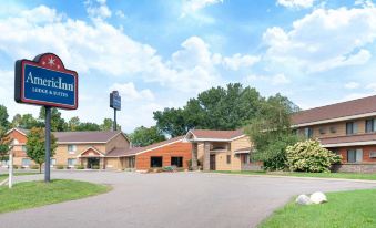 an exterior view of a hotel or motel surrounded by grass and trees , with a sign above the entrance at AmericInn by Wyndham Rogers