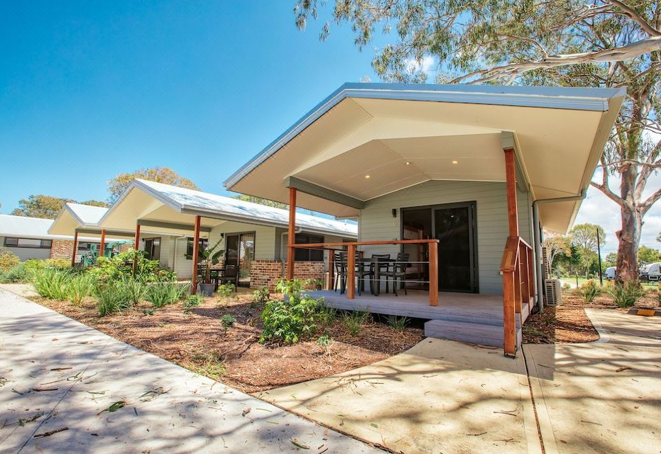 a small , modern house with a curved roof and wooden exterior is surrounded by greenery at BIG4 Sandstone Point Holiday Resort