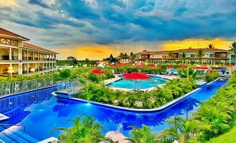 a resort with a large pool surrounded by lounge chairs , umbrellas , and palm trees , under a cloudy sky at Hotel Campestre las Camelias