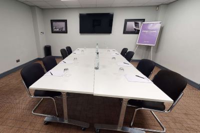 a long table with a white top and black chairs is set up in a room with framed pictures on the wall at Village Hotel Liverpool