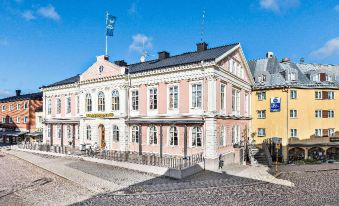 a large , white building with pink and blue trim , located on a cobblestone street in a european city at Vimmerby Stadshotell, WorldHotels Crafted