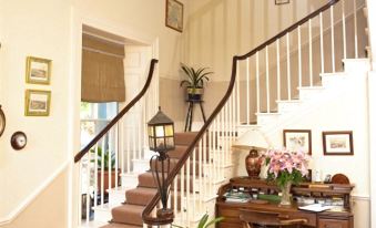 a white staircase with wooden railing , leading to a room decorated with potted plants and flowers at Boulston Manor