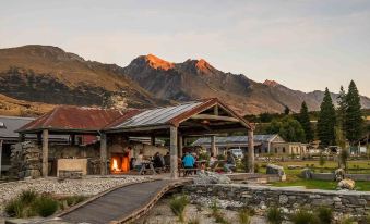 a group of people gathered around a fire pit in the middle of a grassy field , enjoying each other 's company and a warm beverage at The Headwaters Eco Lodge