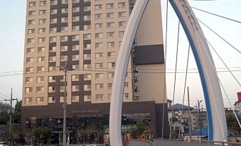 a tall building with a tower , surrounded by a bridge and trees , and a circular metal sculpture in the foreground at Am Hotel