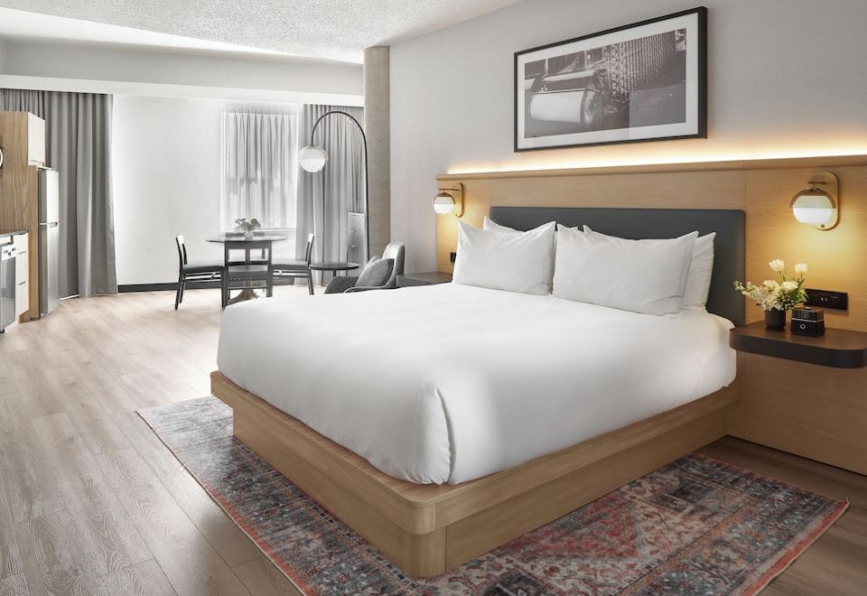 a large bed with white sheets and pillows is in a room with wooden floors , a chair , and a table at Hotel Moco Valleyfield