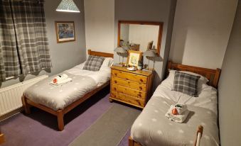 a cozy bedroom with two beds , a dresser , and a mirror , decorated with white towels on the beds at The Village Inn