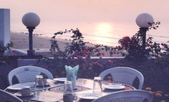 At sunset, there is a table with chairs and an umbrella on the beach, providing a view of the water in front at Hotel Sonali