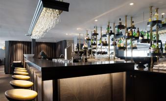 a modern bar with a black countertop , gold chairs , and a chandelier hanging from the ceiling at Scandic Ishavshotel