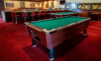 a pool table with a green felt surface is in the middle of a room with red carpet and bar stools at Little America Hotel - Wyoming