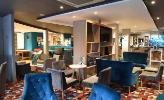 a modern lounge area with blue velvet chairs , a wooden bar , and a bookshelf filled with books at Holiday Inn Glasgow - East Kilbride
