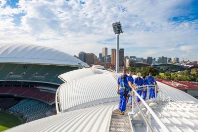 a group of workers in blue uniforms are working on the roof of a stadium at Oval Hotel at Adelaide Oval, an EVT hotel