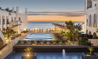 a large swimming pool is surrounded by lounge chairs and a water fountain in front of a hotel at Belmar Spa & Beach Resort