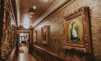 a hallway with gold leaf on the walls , gold - framed pictures on the left and a blue tile floor at Prince of Wales