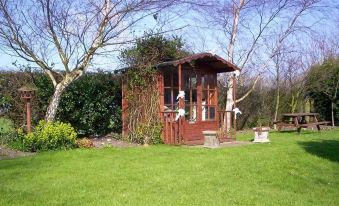 a wooden gazebo surrounded by a lush green lawn , with a bird perched on the railing at St Quintin Arms