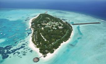 a tropical island surrounded by clear blue water and white sand , with a large resort visible in the distance at Meeru Maldives Resort Island