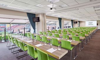 a large conference room filled with rows of green chairs and tables , ready for an event at Lindner Hotel Leverkusen Bayarena