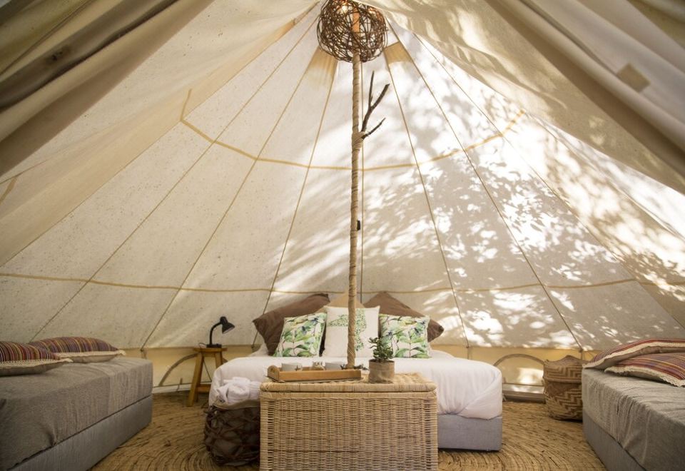 a bed with a white blanket and wicker furniture is in the center of a room with a beige canopy at Niddo Suesca